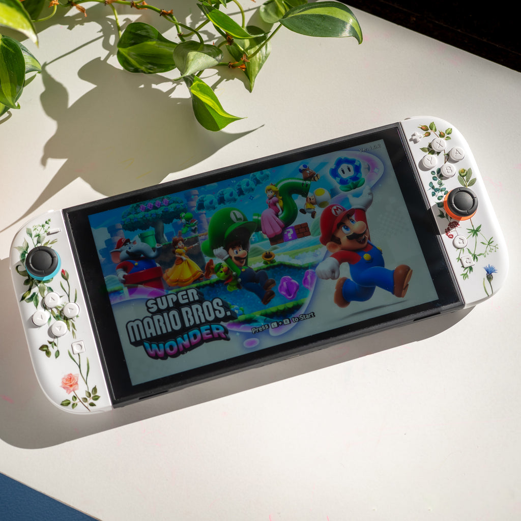 Switch 2 gaming console with floral custom Joy-Cons displaying 'Super Mario Bros. Wonder' game on a light surface with a plant in the background.